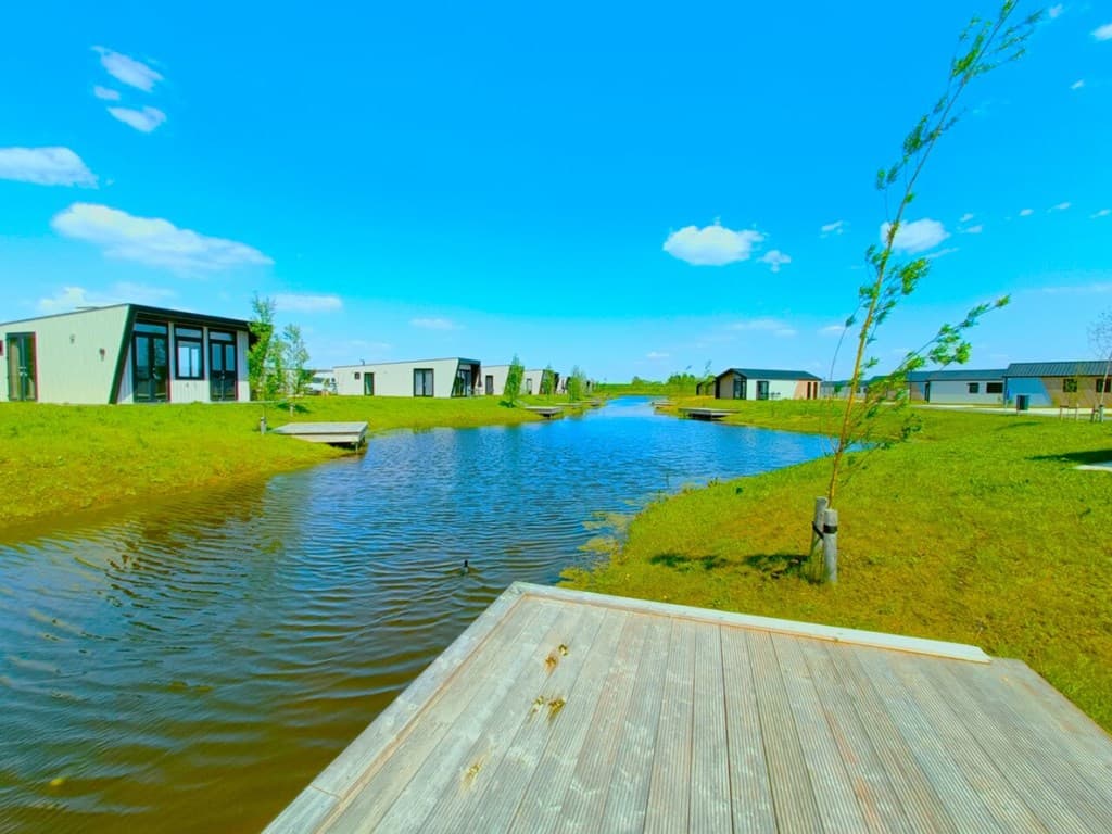Uitzicht over een waterpartij omringd door vakantiewoningen, met een heldere blauwe lucht en groene grasvelden.