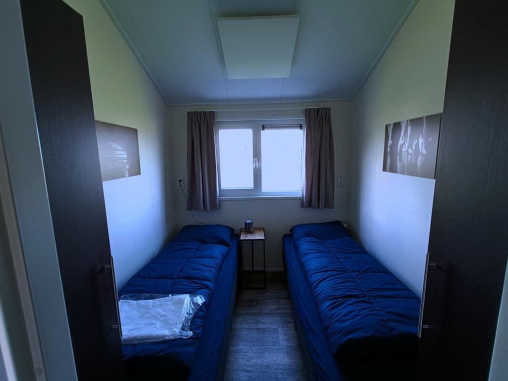 Slaapkamer met twee eenpersoonsbedden, een nachtkastje en een raam met gordijnen.