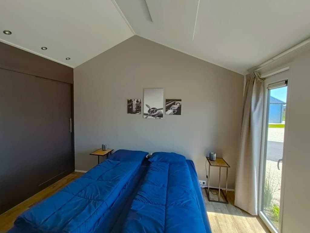 Sfeervolle slaapkamer met twee blauwe bedden, nachtkastjes en een deur naar buiten met uitzicht op de tuin.
