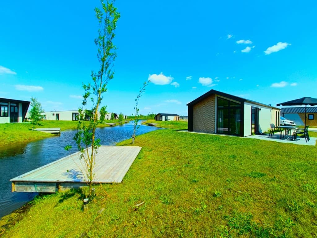 Moderne vakantiewoning aan water met een houten aanlegsteiger, omgeven door groen en andere woningen op EuroParcs De IJssel E