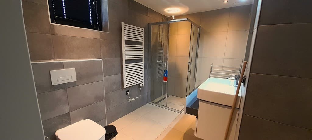 Moderne badkamer met een inloopdouche, wastafel, toilet en handdoekenradiator in grijstinten.