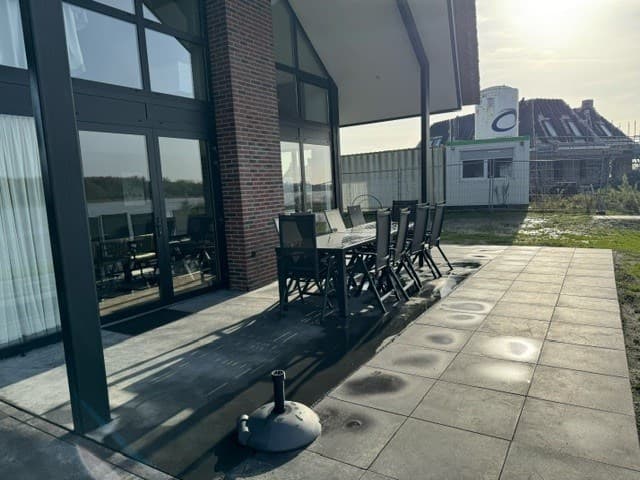 Terras met eettafel en stoelen, zicht op de achtertuin en een gebouw in aanbouw op de achtergrond