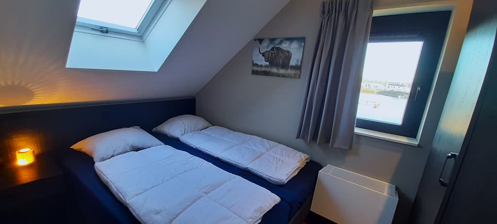Slaapkamer met twee aparte bedden, een raam met uitzicht en een schilderij aan de muur