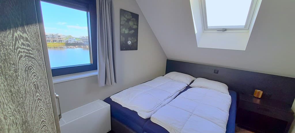 Slaapkamer met een tweepersoonsbed, raam met uitzicht op water en moderne inrichting, lichte muren en houten details