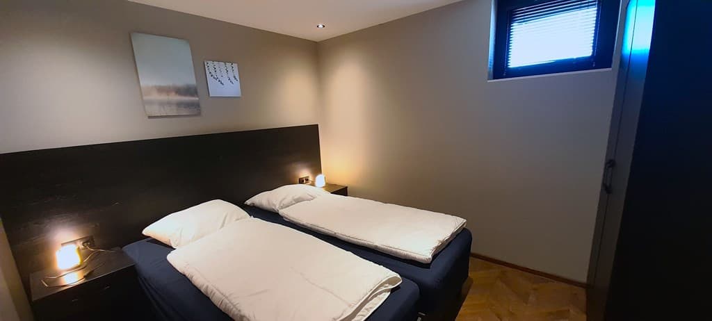 Slaapkamer met twee eenpersoonsbedden, nachtkastjes met lampen en een raam met jaloezieën.