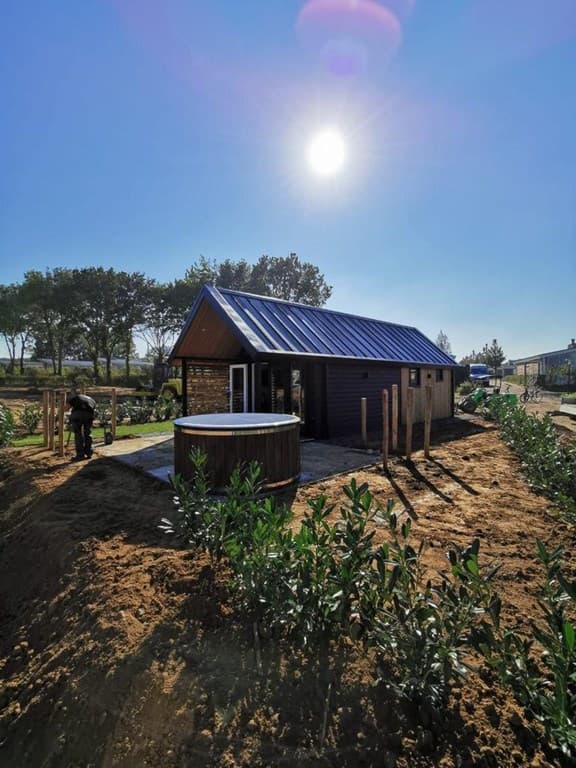 Moderne vakantiewoning met schuine dak, omgeven door groen en een terras met een houten hottub in de zon.