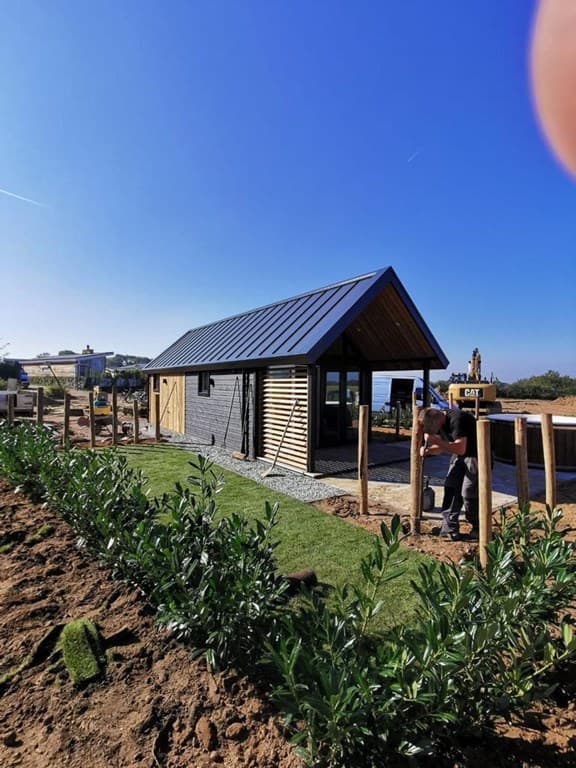 Moderne vakantiewoning met zwart houten gevel, een schuin dak en een groene tuin in een zonnige omgeving.