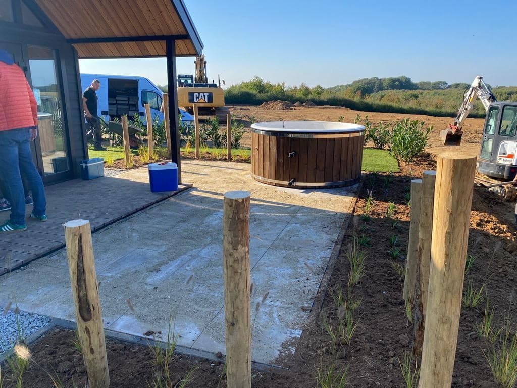 Tegenwoordig is er een patio met een houten jacuzzi en houten palen rondom, met uitzicht op een open landschap.