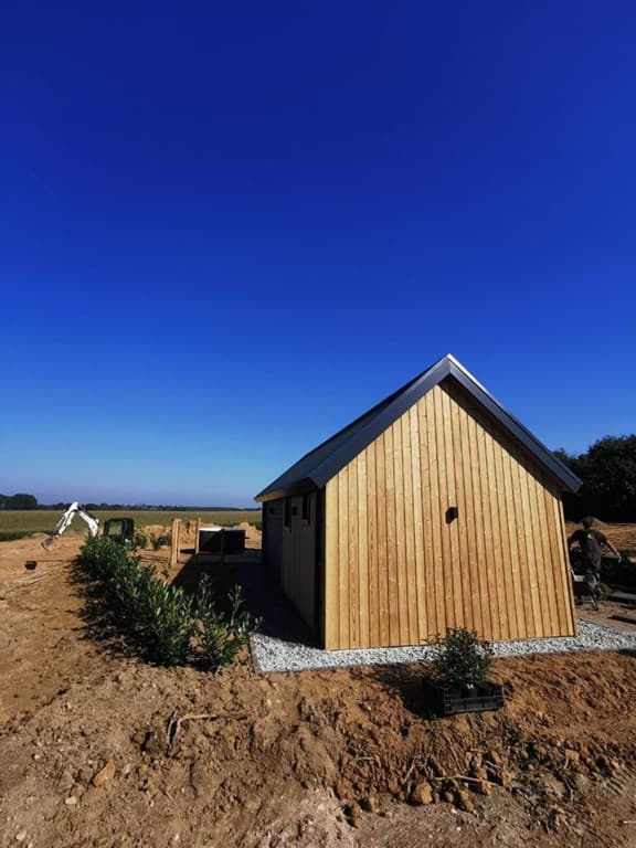 Houten vakantiewoning met een hellend dak en een blauwe lucht op de achtergrond, omgeven door een onbewerkte omgeving.