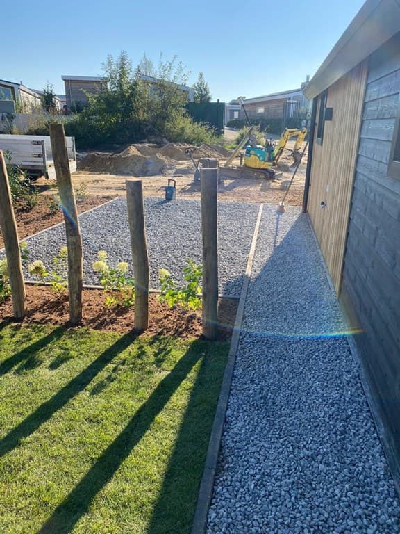 Grasveld met grindpad, houten schutting en speeltoestellen op een zonnige dag in Green Resort Mooi Bemelen.