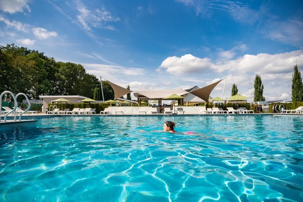 Zwemmer in een helderblauw zwembad met ligstoelen en parasols op de achtergrond onder een heldere lucht