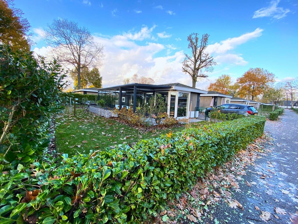 Vakantiehuis met tuin omringd door heg, gelegen in EuroParcs Limburg, met bomen en een heldere lucht op de achtergrond