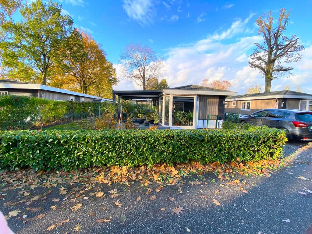 Buitenzicht op een vakantiewoning met overdekt terras en omringende groene haag in een rustige omgeving met bomen.