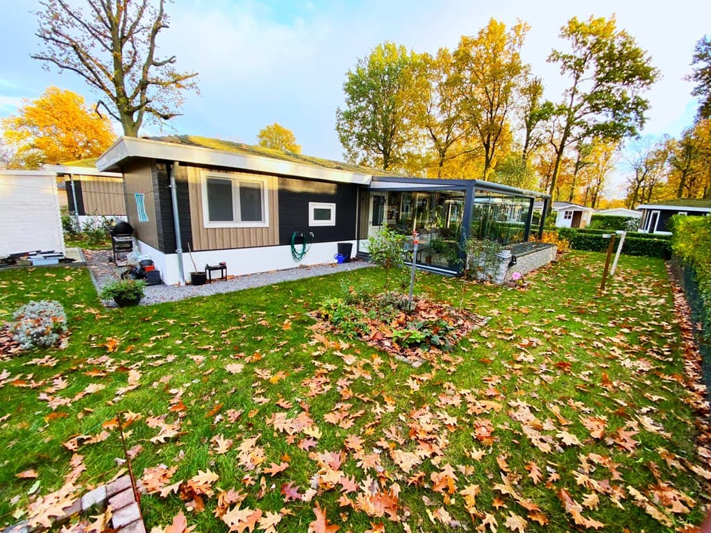 Moderne woning met een tuin vol bladeren en een overdekt terras, omgeven door bomen.