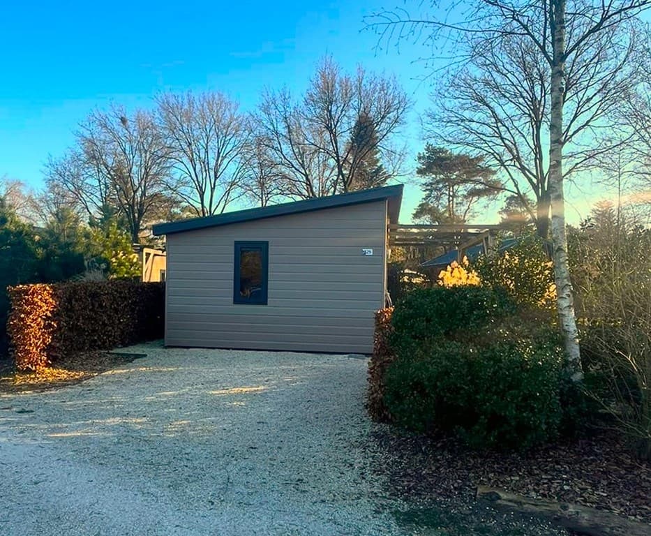 Moderne vakantiewoning met een houten façade en grote ramen, omgeven door beplanting en gravelpad in EuroParcs De Wije Werelt