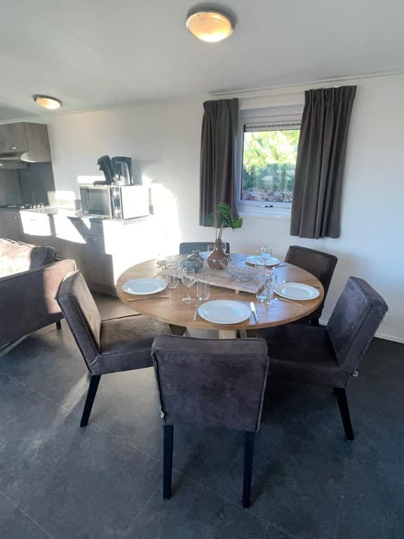 Eethoek met ronde tafel, vier stoelen, en servies in een moderne woonkamer met raam en sfeervolle verlichting