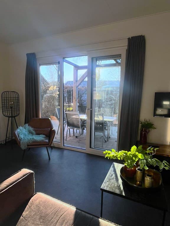 Woonkamer met grote glazen deuren naar een terras, een comfortabele stoel en een plant op een tafel