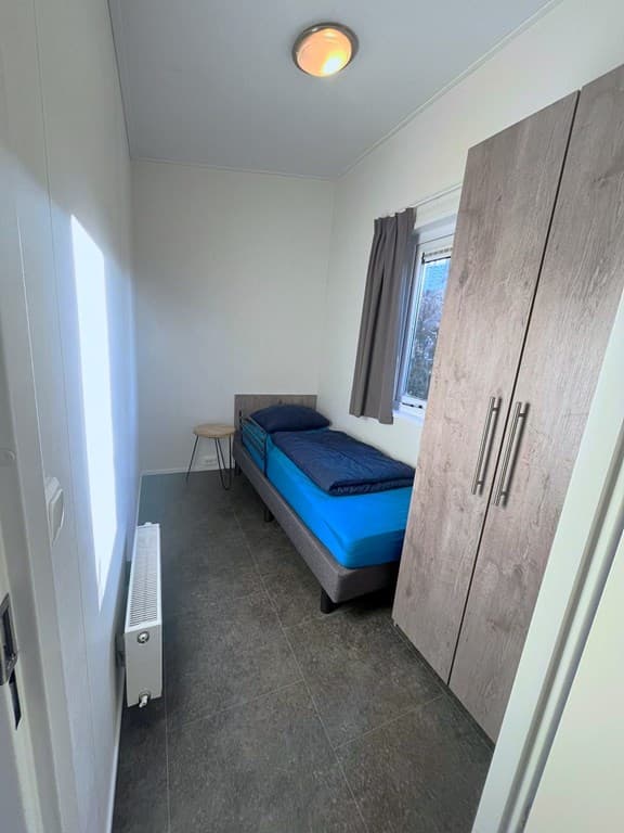 Slaapkamer met een eenpersoonsbed, kast, tafeltje en raam met zicht naar buiten