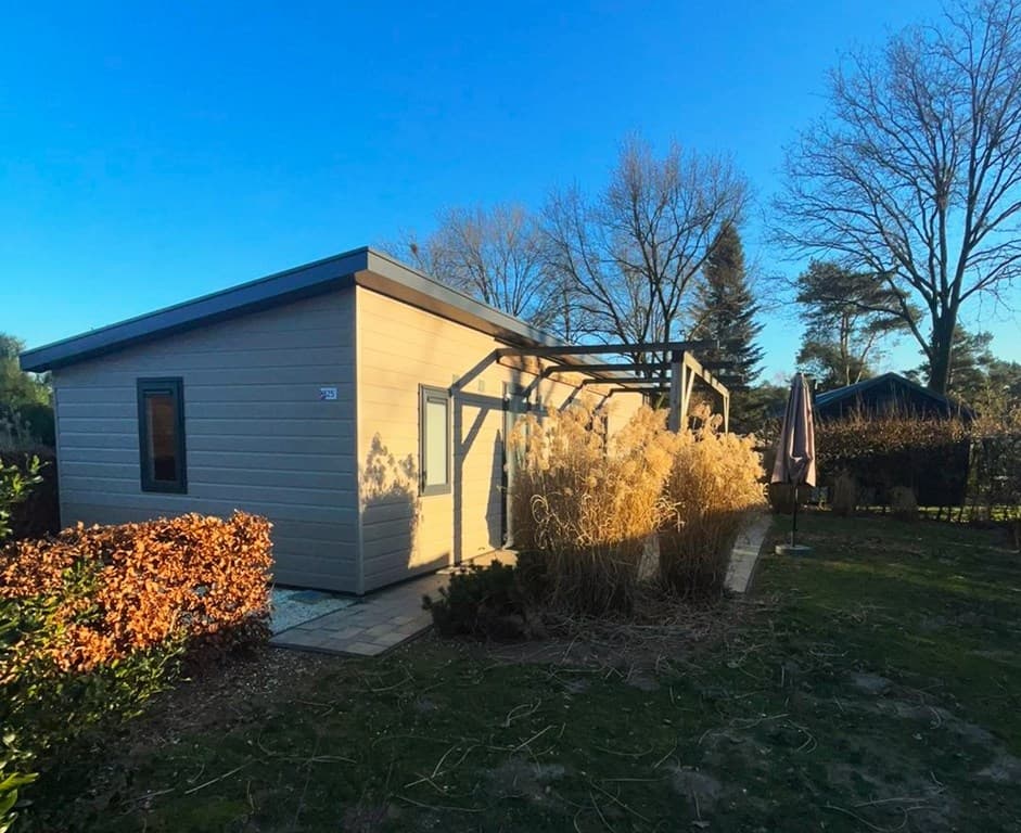 Vakantiewoning met een moderne uitstraling, gelegen in een groenrijke omgeving met struiken en een patio.