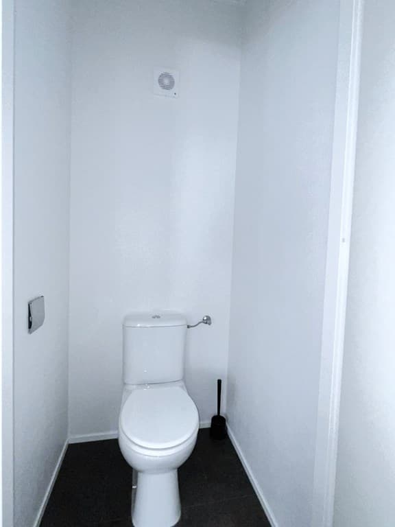 Witte toiletruimte met een toilet en een toiletborstel, muren en vloer in neutrale kleuren