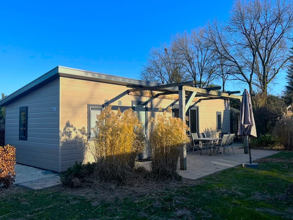 Moderne vakantiewoning met overdekt terras en tuintafel, omringd door groene begroeiing en kastanjebomen.