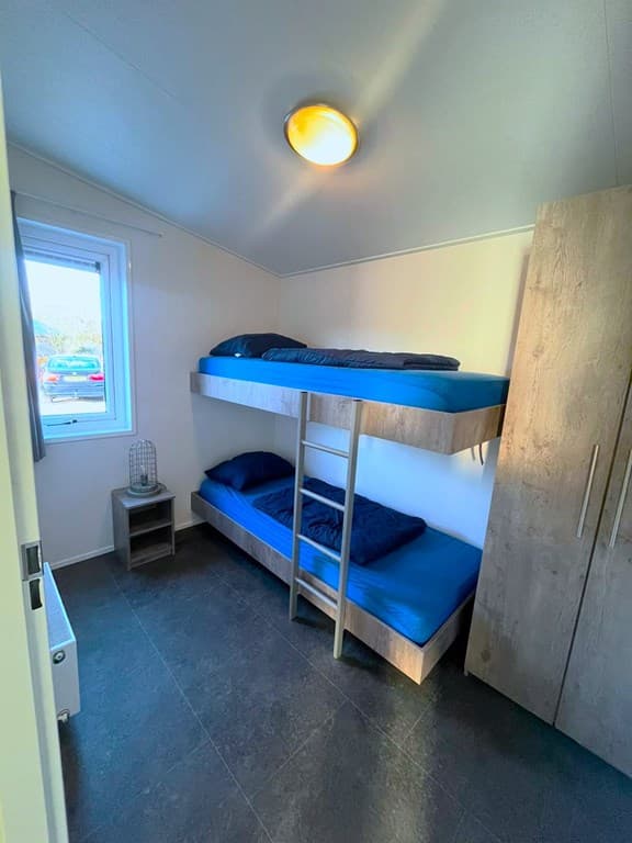 Slaapkamer met stapelbed en kasten, verlichte ruimte met vloerbedekking en raam naar buiten.