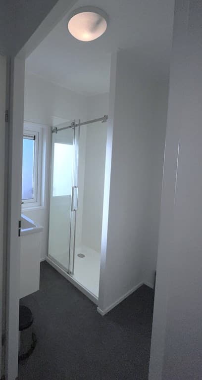 Moderne badkamer met douchecabine, wastafel en raampje voor natuurlijke lichtinval.