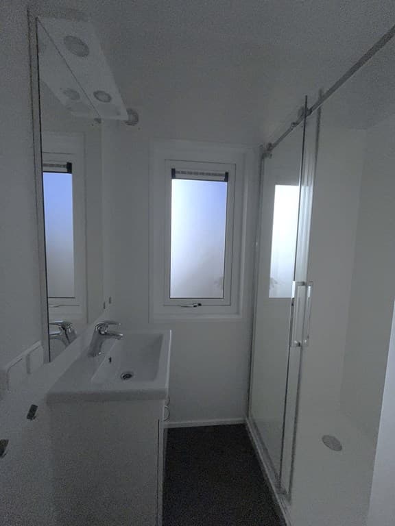 Badkamer met douchecabine, wastafel en raam met uitzicht naar buiten. Minimalistisch en licht interieur.