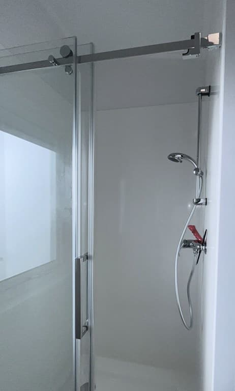 Moderne douchecabine met glazen deuren en ronde handdouche in lichte ruimte