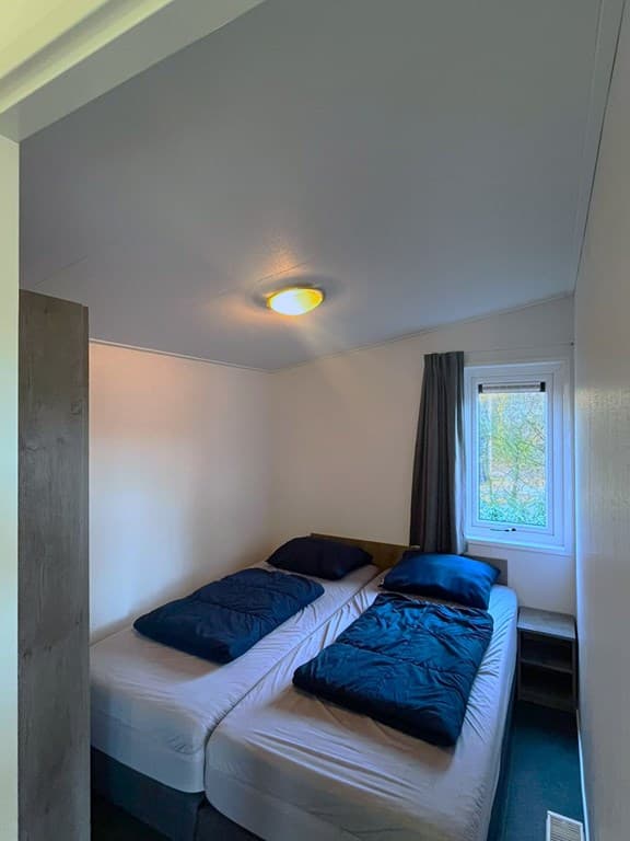 Slaapkamer met twee eenpersoonsbedden, raam met gordijn en een lamp aan het plafond.