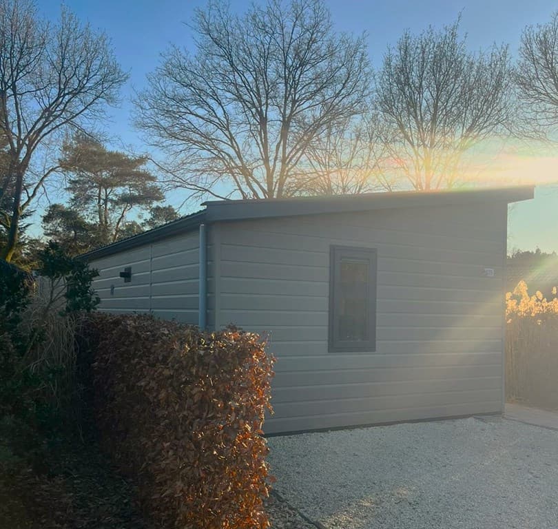 Moderne vakantiewoning met een lichte gevel, omringd door bomen en een fraaie haag, gelegen in een groene omgeving