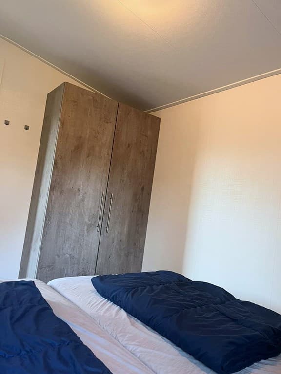 Slaapkamer met een bed met een navy dekbed en een houten kast tegen de muur.