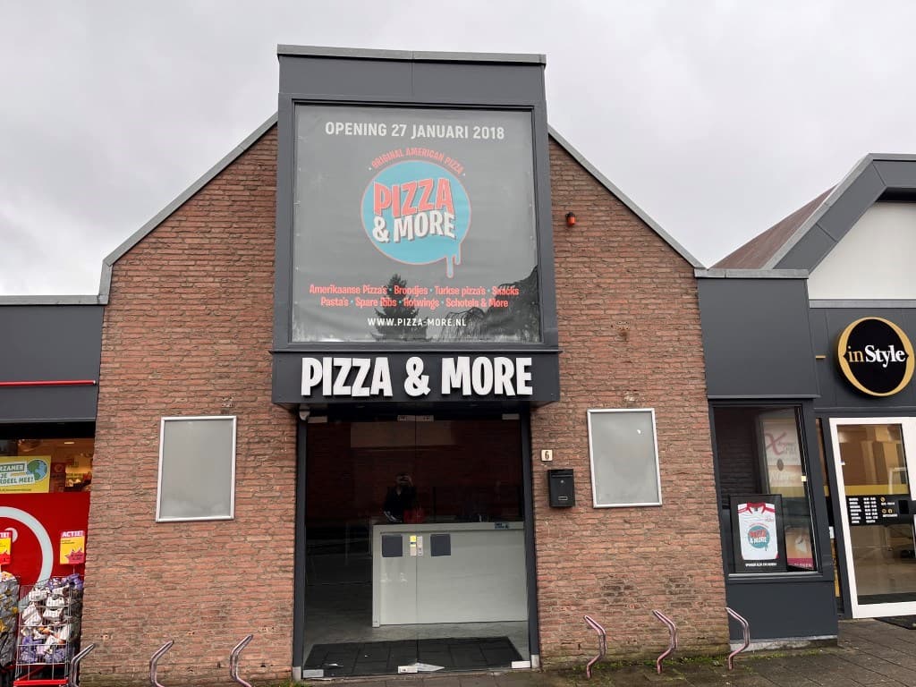 Gevel van een restaurant met een grote gevelsignering en een ruime ingangsdeur, omgeven door andere winkels