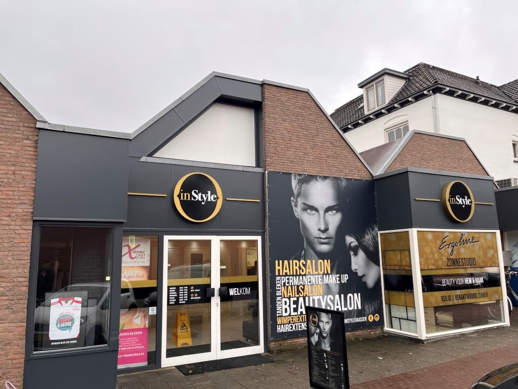 Voorkant van een modern gebouw met een kapsalon en beautysalon, grote ramen en een reclamebord met een model.