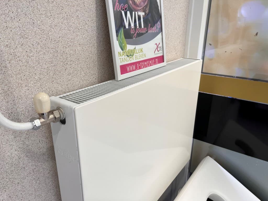 Witte verwarming aan de wand met een poster erboven in een ruimte met een lichte wand.