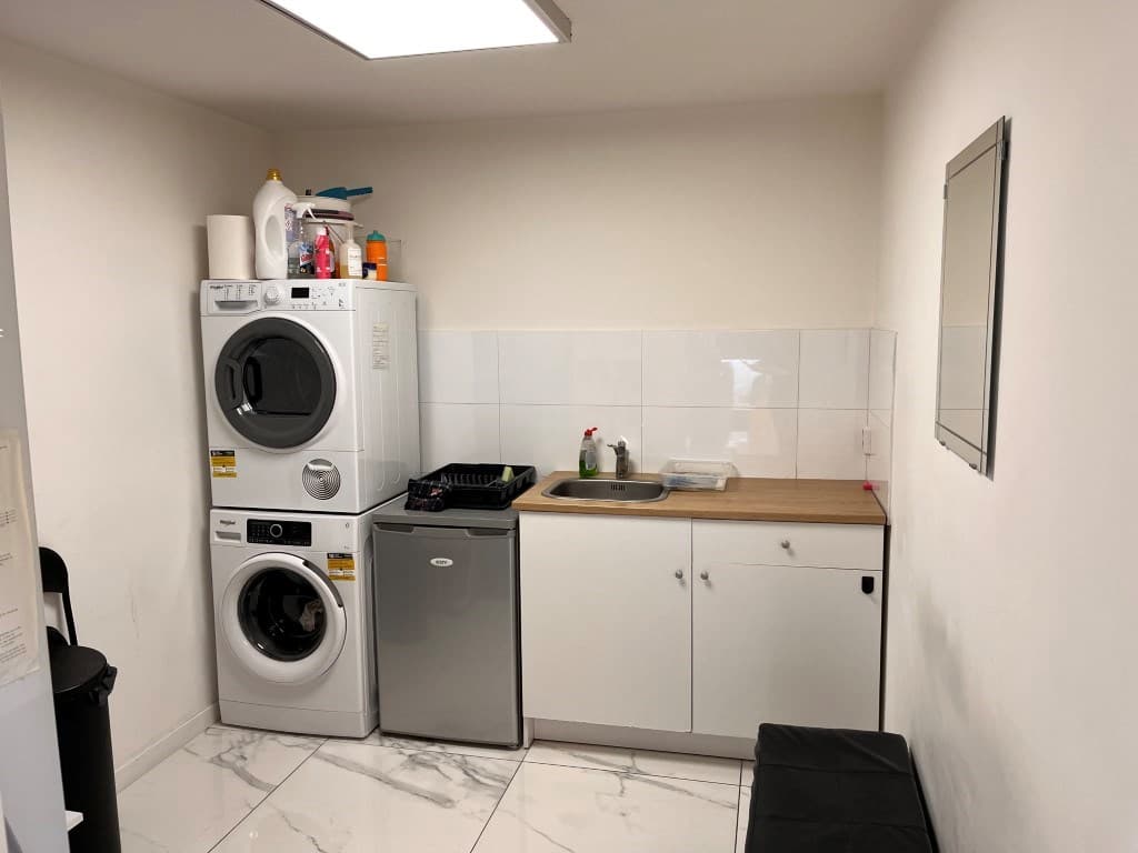 Keuken met wasmachine, droger, aanrecht, gootsteen en een koelkast in een appartement