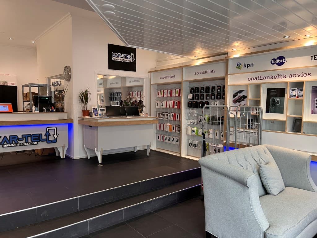 Toon van een winkelruimte met een receptie, diverse accessoires en telefoons op schappen, en een zitgedeelte met een grijze b