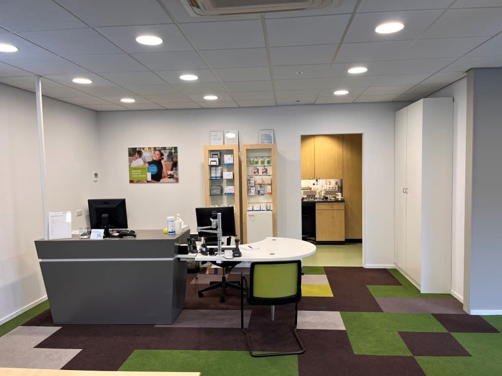 Ingerichte receptie van een appartement met bureau, stoelen en open keuken in de achtergrond.