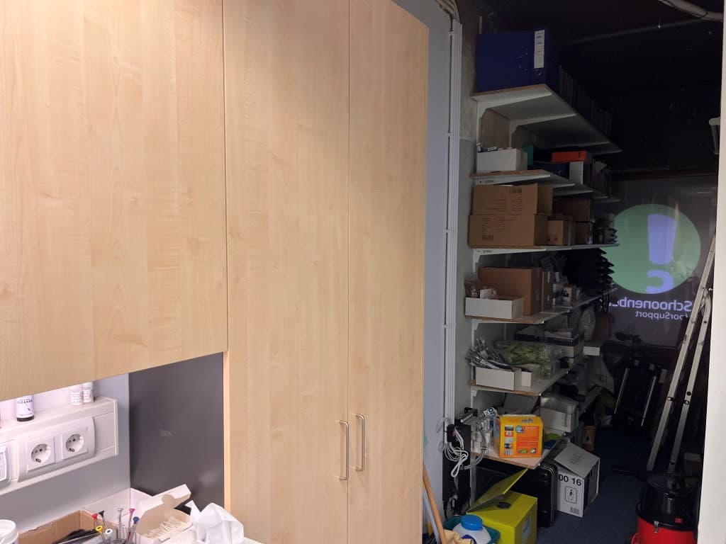Ingerichte ruimte met houten kasten en planken vol spullen tegen de muur, helder verlicht met een projector op de achtergrond