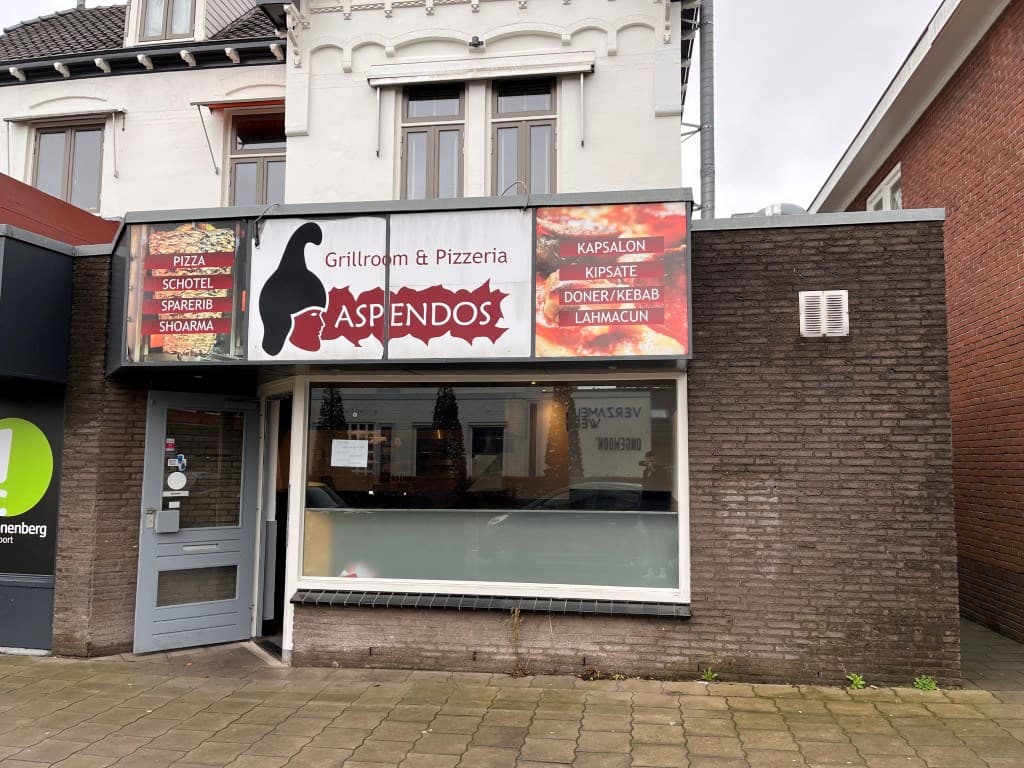 Voorgevel van het restaurant Aspendos met grote ramen en een geveldecoratie in een rustige straat.