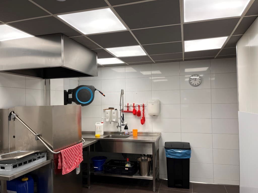 Keuken met metalen apparatuur, spoelbak, klokken en een paar rode keukengerei aan de muur