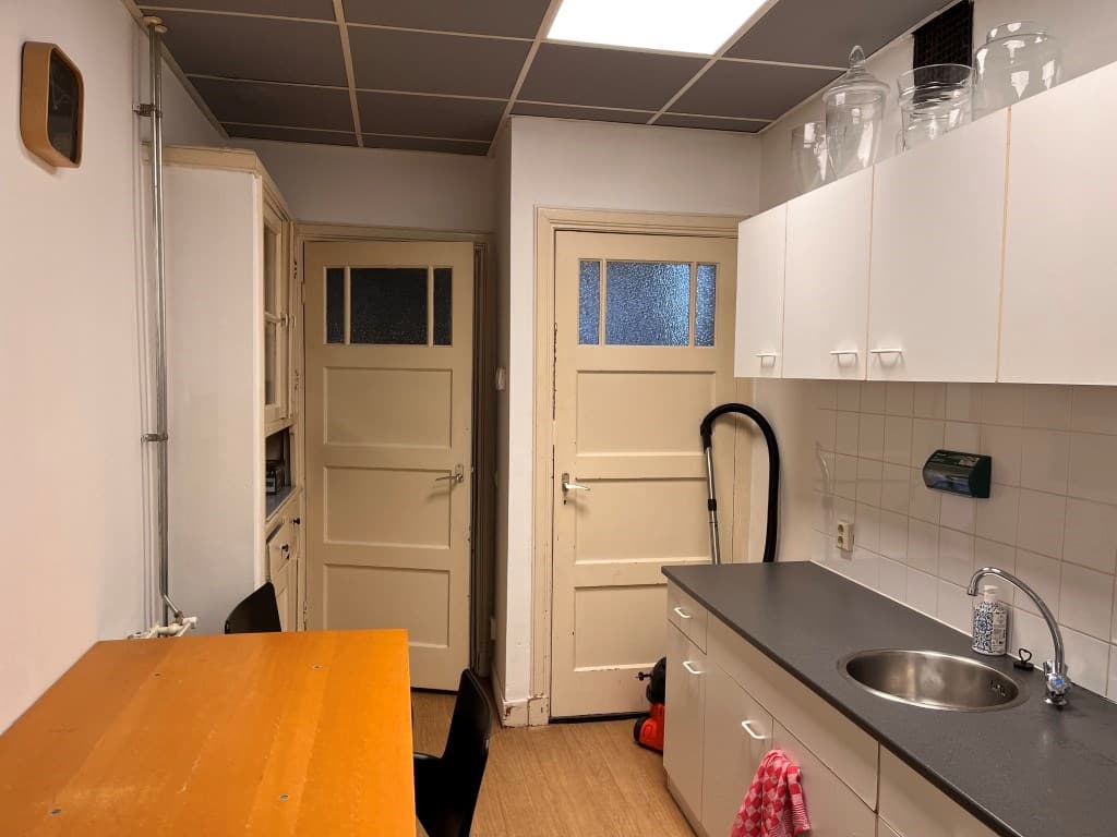 Keukenruimte met een tafel en stoelen, kasten, aanrecht met spoelbak en twee deuren naar aangrenzende ruimtes.