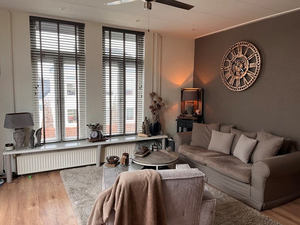 Bedrijfsruimte met zithoek, grote ramen met jaloezieën en decoratieve muurdetails.