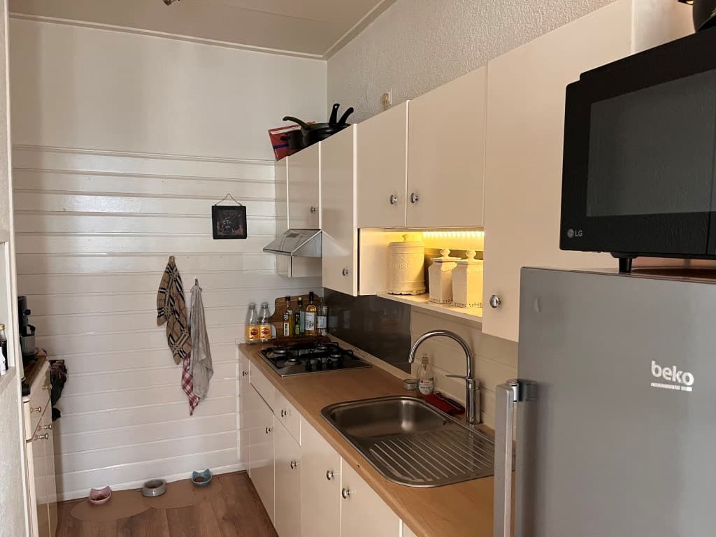 Keuken met beige kastjes, kookplaat, wasbak en diverse flessen op het aanrecht in een appartement.