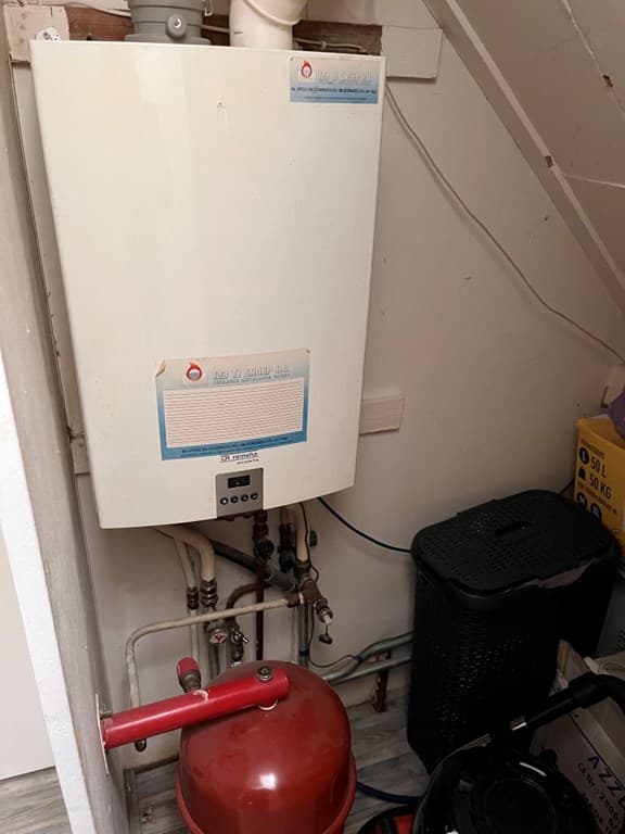 Foto van een warmwaterinstallatie met een rode drukfles en diverse leidingen in een technische ruimte.