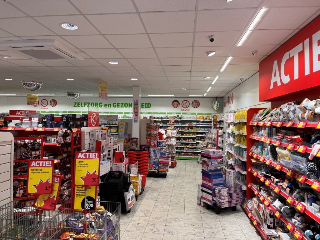 Interieur van de winkel met schappen vol artikelen en een gangpad, inclusief promotionele displays en betonnen vloer.