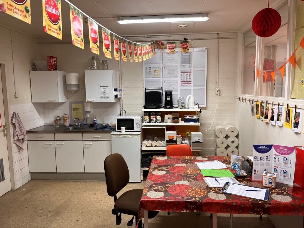 Keuken met tafeltje, stoelen, materialen en apparatuur, waaronder een magnetron en een koelkast, in een lichte ruimte