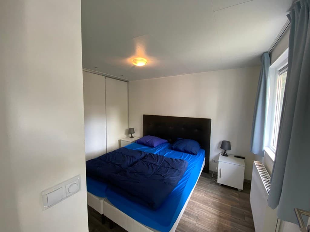 Slaapkamer met een tweepersoonsbed, nachtkastjes en een raam met gordijnen in een vakantiewoning.
