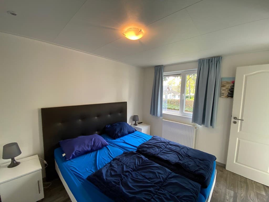 Slaapkamer met een dubbelbed, nachtkastjes, raam met gordijnen en een radiator zichtbaar aan de muur