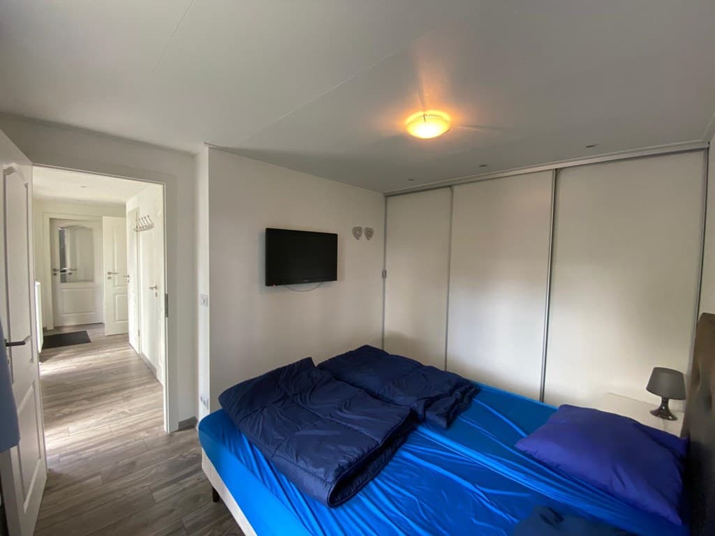 Slaapkamer met een tweepersoonsbed, muurkast, een televisie en toegang tot een hal met spiegel en deuren.